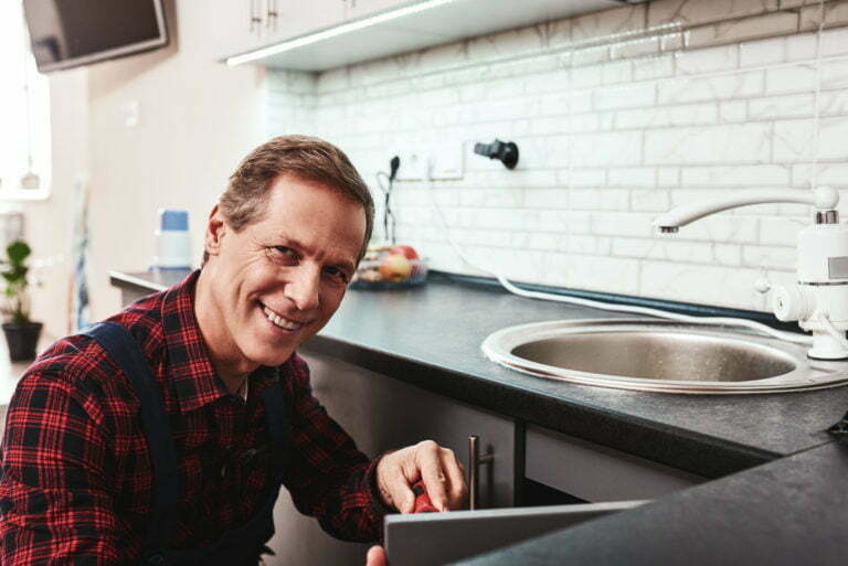 Smiling master. Seniour handyman repairing washbasin with smile