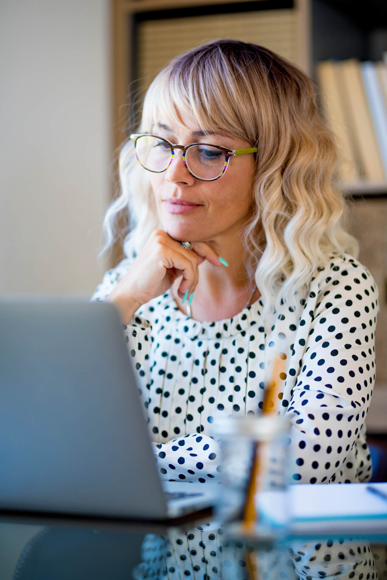 a woman sitting at a table with a laptop and pen in her hand